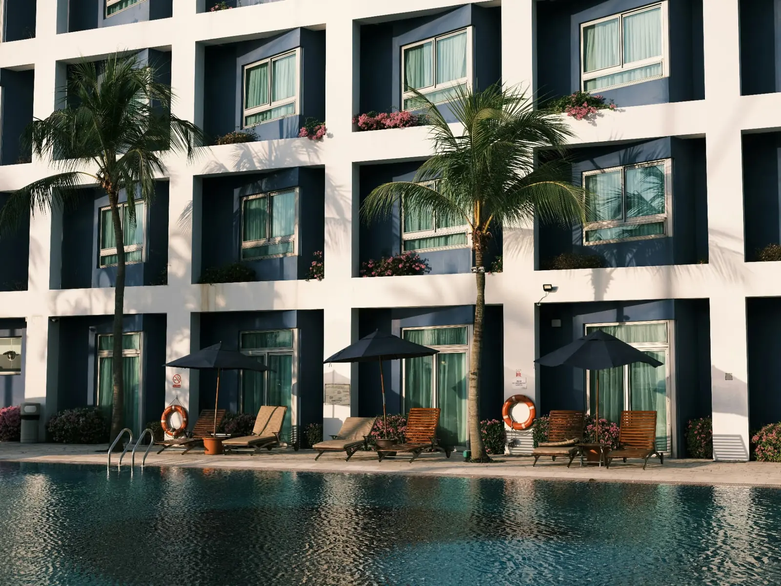 Resort pool deck with palm trees and modern white hotel facade