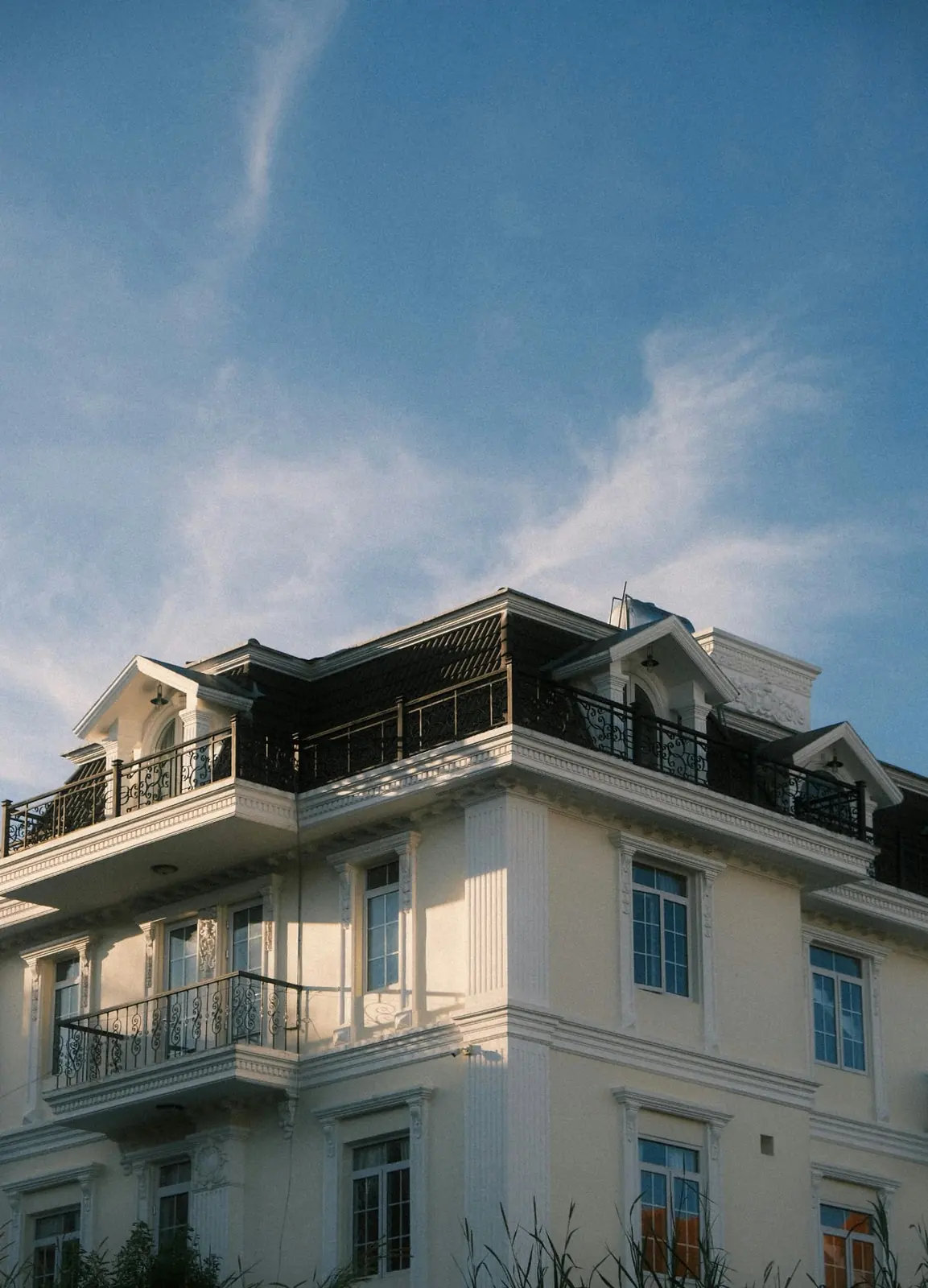 Elegant real estate property exterior with classical architecture and balconies against a blue sky